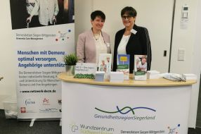 Zwei Frauen stehen an einem Informationsstand zum Thema Demenzversorgung in der Gesundheitsregion Siegenland.