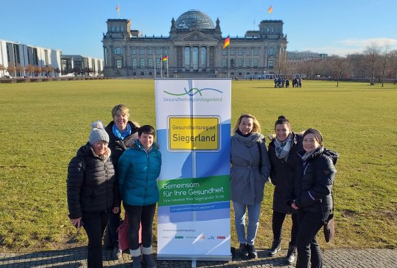 Eine Gruppe von Frauen steht lächelnd vor einem Banner der Gesundheitsregion Siegerland vor dem Reichstagsgebäude.