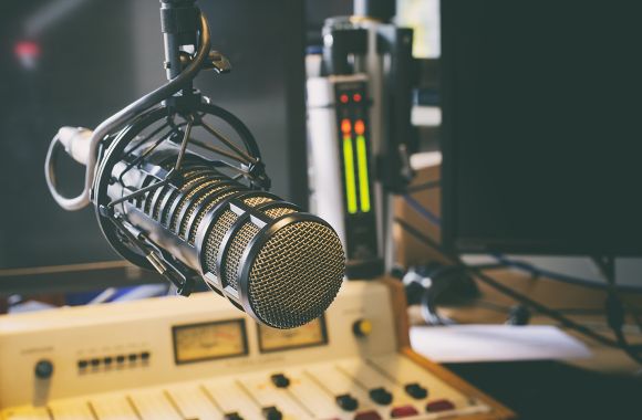 Ein Mikrofon hängt in einem modernen Radiostudio über einem Mischpult mit verschiedenen Bedienelementen.