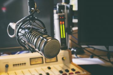 Ein Mikrofon hängt in einem modernen Radiostudio über einem Mischpult mit verschiedenen Bedienelementen.