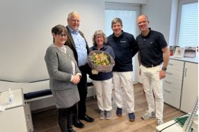 Fünf Personen in einem Behandlungsraum posieren lächelnd mit einem Blumenstrauß. Auf dem Bild zu sehen: Anja Herder-Peyrounette, Dr. Harald Menker, Dorothee Massing,  Dr. Stergios Tsolakidis, Dr. Wilhelm Litz