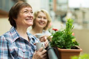 Zwei Frauen stehen lächelnd auf dem Balkon, während sie Tassen halten.